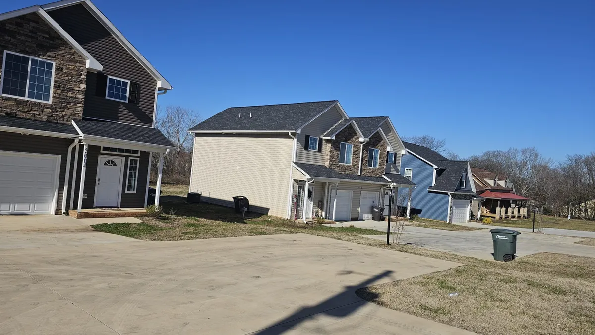 An exterior view displays the duplex building with a well-maintained driveway and clear blue sky, hinting at the available on-site parking and the property's approachable neighborhood setting.