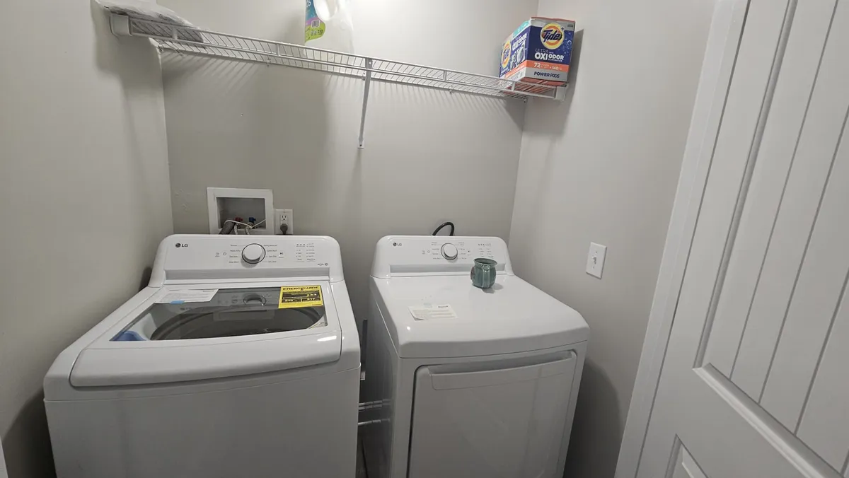 A dedicated laundry area is shown here, featuring a washing machine and dryer neatly stacked beneath a shelf stocked with detergent. The setting is practical and organized, evoking the ease of handling daily chores within the home.