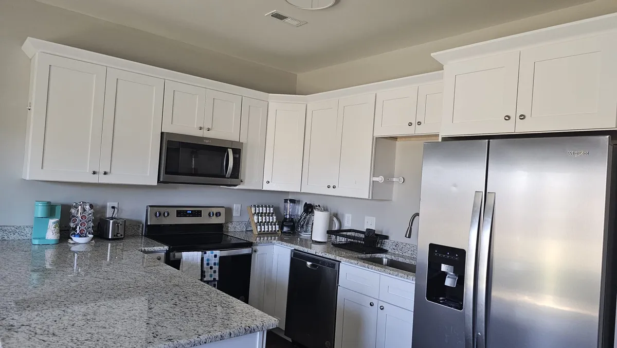 A spacious, modern kitchen featuring sleek granite countertops, stainless steel appliances, and pristine white cabinetry. The layout is open and functional, providing ample counter space for meal preparation and easy movement, perfect for both cooking and entertaining.
